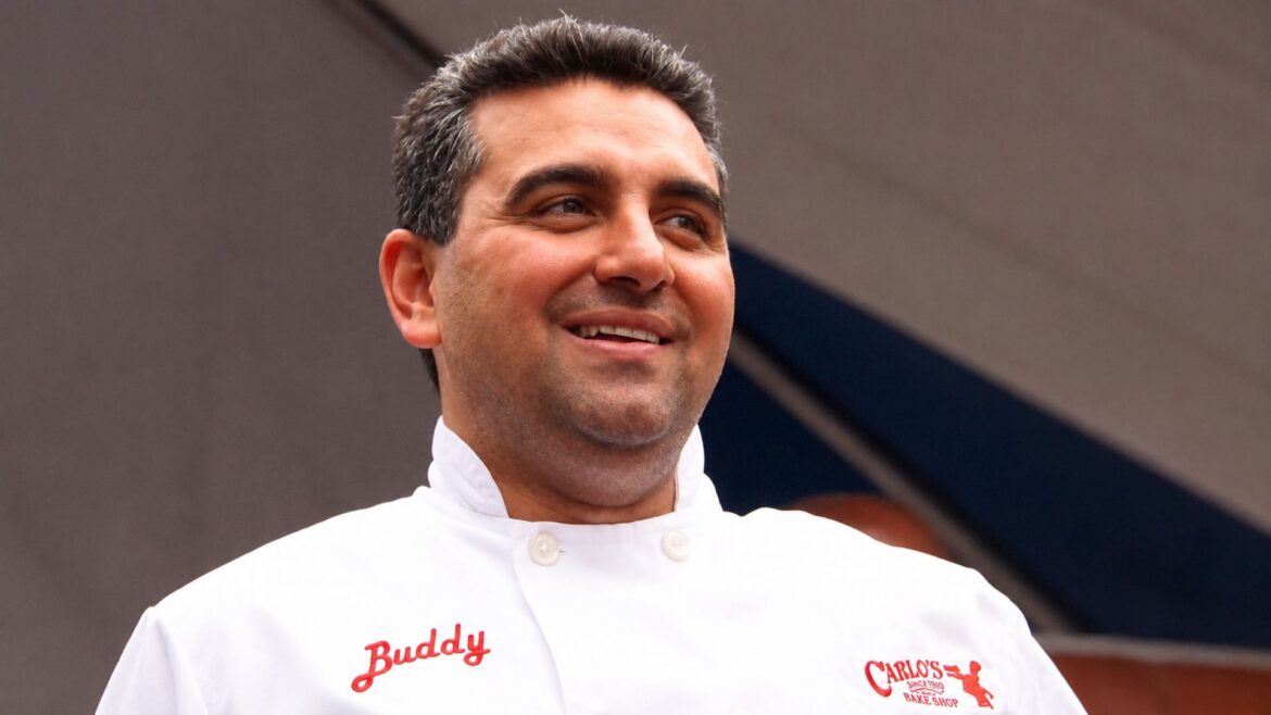 Buddy Valastro wearing his white Carlo's Bakery chef jacket and smiling during a public appearance.